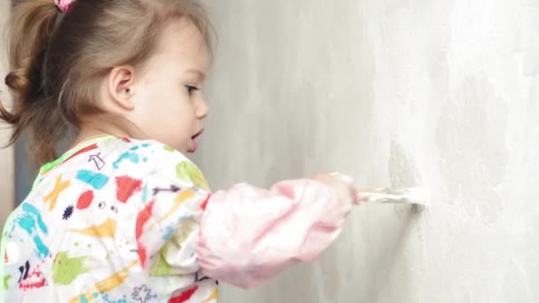 Reparación, renovación, hogar, familia, infancia, paternidad, paternidad, autoaislamiento, concepto de cuarentena: primer plano niña de 3 años jugando con el rodillo, pintando la pared en la pintura blanca del apartamento . — Vídeos de Stock