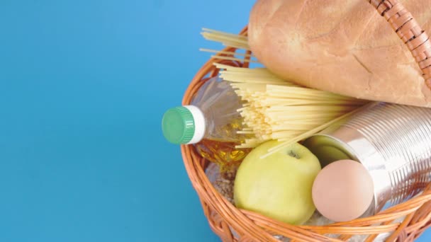 Donation, alms, healthy nutrition, humanitarian aid, pandemic, Covid-19 concept. Closeup male left hand in a white medical glove lays an apple in a wicker basket with food on a classic blue background — Stock Video