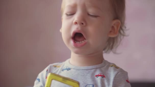 Infancia, ocio, juego, auto-aislamiento, tecnología, concepto de comunicación - primer plano lindo niño de dos años de pelo rubio gritando sonriente lanza juguetes y demuestra emociones divertidas en el dormitorio . — Vídeo de stock