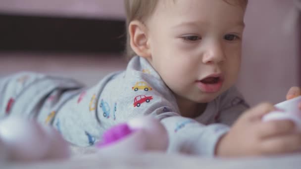 童年、闲暇、游戏、自我封闭、科技、交流理念- -快乐可爱的两岁金发男孩躺在床上玩塑料蛋. — 图库视频影像