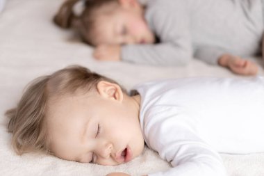 Çocukluk, uyku, rahatlama, aile, yaşam tarzı konsepti - 2 ve 3 yaşlarındaki iki genç, beyaz ve bej giysiler içinde öğle yemeğinde el ele tutuşarak bej ve beyaz bir yatakta uyurlar..