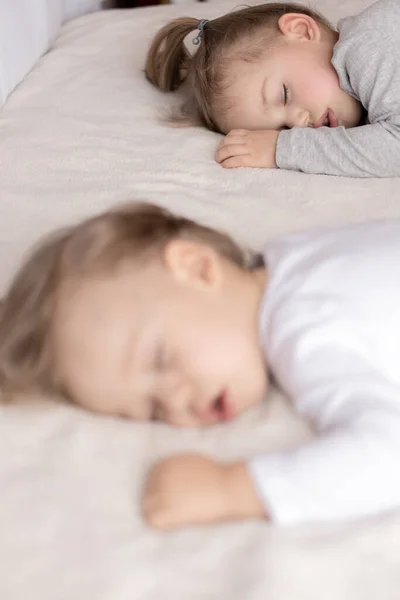Childhood, sleep, relaxation, family, lifestyle concept - two young children 2 and 3 years old dressed in white and beige bodysuit sleep on a beige and white bed at lunch holding hands top view. — Stock Photo, Image