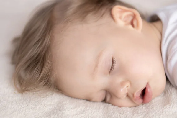Enfance, sommeil, repos, famille, mode de vie - portrait en gros plan d'un mignon petit garçon de 2 ans dans un corps blanc dormant sur un lit beige à midi avec bouche ouverte et vue latérale . — Photo