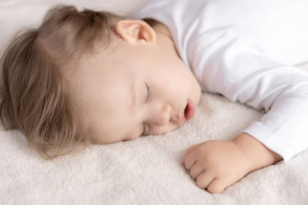 Enfance, sommeil, repos, famille, mode de vie - portrait en gros plan d'un mignon petit garçon de 2 ans dans un corps blanc dormant sur un lit beige à midi avec bouche ouverte et vue latérale . — Photo