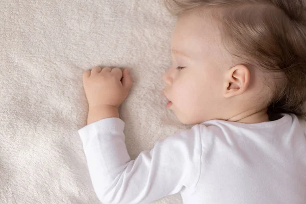 Enfance, sommeil, repos, famille, mode de vie - portrait en gros plan d'un mignon petit garçon de 2 ans dans un corps blanc dormant sur un lit beige à midi avec bouche ouverte et vue latérale . — Photo