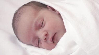 çocukluk, çocukluk, ebeveynlik, annelik konsepti - beyaz bej bir yatağa sarılı yeni doğmuş bir bebeğin yakın plan portresi uyanıyor uyanıyor gözlerini açıyor ve dilini çıkarıyor.