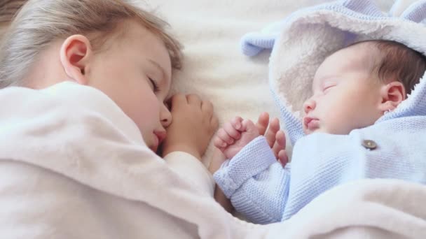 Infância, infância, família, sono, conceito de descanso - close-up de duas crianças, bebê recém-nascido e menina de três anos dormindo juntos em uma cama bege e branca. Irmãs estão dormindo no sofá em casa . — Vídeo de Stock