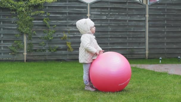 Infanzia, tempo libero, gioco, cortile, concetto primaverile - tre bambini piccoli giocano nel cortile con le palle e un fitball su un'erba verde all'inizio della primavera con il freddo . — Video Stock