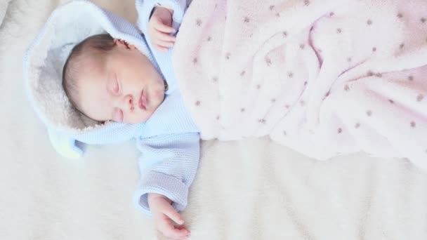 Infancia, infancia, paternidad, maternidad, concepto familiar - vista superior de un bebé recién nacido dormido en pleno crecimiento acostado horizontalmente en blusa azul y cubierto con una manta rosa sobre un fondo blanco . — Vídeos de Stock