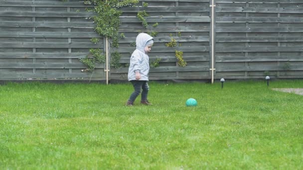 Jeugd, vrije tijd, spel, tuin, lente concept - drie jonge kinderen spelen in de tuin met ballen en een fitbal op een groen gras in het vroege voorjaar bij koud weer. — Stockvideo