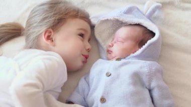 Çocukluk, çocukluk, aile, uyku, dinlenme konsepti - iki çocuğa yakın çekim, yeni doğan bebek ve üç yaşındaki kız bej ve beyaz bir yatakta birlikte uyuyorlar. Kız kardeşler evdeki kanepede yatıyorlar..