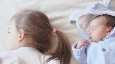 Çocukluk, çocukluk, aile, uyku, dinlenme konsepti - iki çocuğa yakın çekim, yeni doğan bebek ve üç yaşındaki kız bej ve beyaz bir yatakta birlikte uyuyorlar. Kız kardeşler evdeki kanepede yatıyorlar..