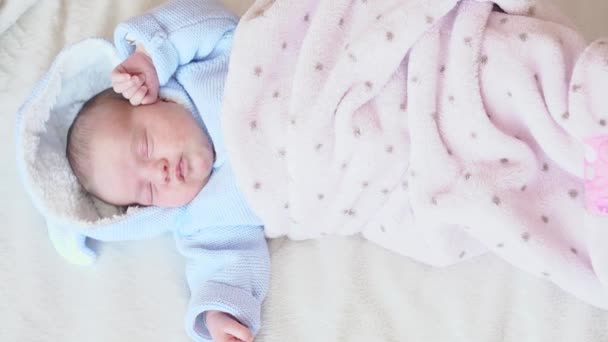 Infanzia, infanzia, genitorialità, maternità, concetto di famiglia - vista dall'alto di un neonato addormentato in piena crescita sdraiato orizzontalmente nella camicetta blu e coperto da una coperta rosa su uno sfondo bianco . — Video Stock