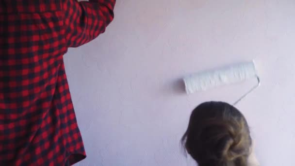 Hermosa pareja decorar su nuevo apartamento y tontos alrededor. Esposo y esposa están pintando la pared con rodillos que se sumergen en pintura azul claro. Son felices y se divierten. Renovaciones en casa — Vídeo de stock