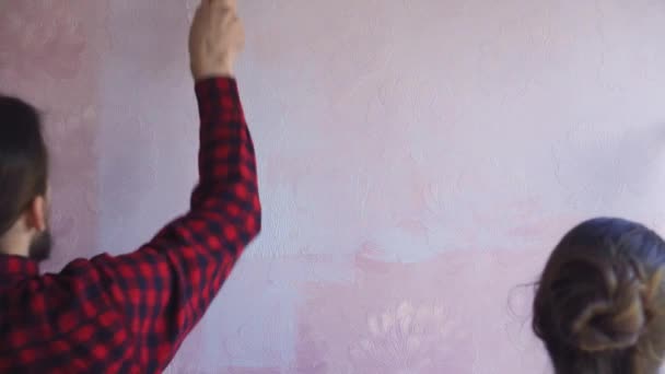 Krásný pár zdobí jejich nový byt a blázen kolem. Manžel a manželka malují stěnu válečky, které jsou namočené ve světle modré barvě. Jsou šťastní a bavte se. Renovace doma — Stock video