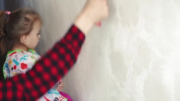 Reparación, renovación, hogar, familia, infancia, paternidad, paternidad, autoaislamiento, concepto de cuarentena: primer plano niña de 3 años jugando con el rodillo, pintando la pared en la pintura blanca del apartamento . — Vídeos de Stock