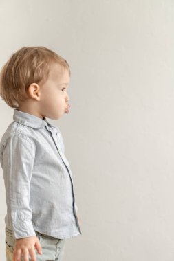 Çocukluk, duygu konsepti - orta sınıf plan. Gri tişörtlü, sarı saçlı, tatlı bir çocuğu izole et. Beyaz bir arka planda suratını ekşittiğini gösteriyor..