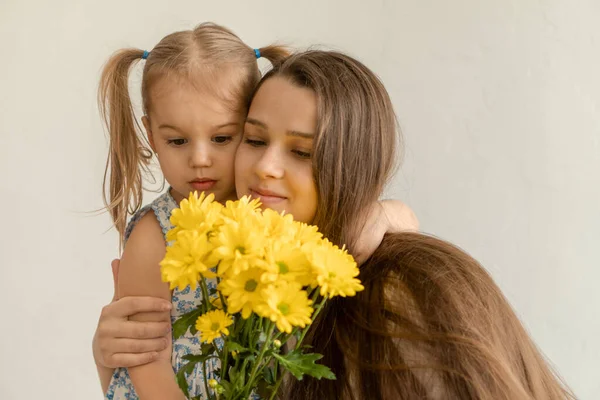 Материнство, День матери, день рождения, детство, семейная концепция - крупным планом малышка в синем красочном платье поздравляет и дарит молодой маме яркий букет желтых ромашковых цветов. — стоковое фото