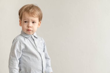 Çocukluk, duygu konsepti - orta plan. Gri tişörtlü, sarı saçlı küçük şirin bir çocuğu izole et. Beyaz arka plan fotokopisinde suratını buruşturuyor..