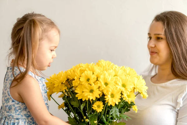Μητρότητα, ημέρα της μητέρας, γενέθλια, παιδική ηλικία, έννοια της οικογένειας - close-up κοριτσάκι σε μπλε πολύχρωμο φόρεμα συγχαρώ και να δώσει νεαρή μητέρα φωτεινό μπουκέτο από κίτρινα λουλούδια μαργαρίτα. — Φωτογραφία Αρχείου