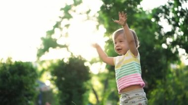 çocukluk, aile, yaşam tarzı, eğlence ve insan konsepti. Renkli tişörtlü, çimenleri yırtan ve gün batımına karşı parka kusan iki yaşında tatlı bir çocuk. yavaş çekim