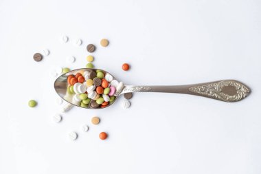 İlaç ve sağlık, ilaç, ilaç, koronavirüs, salgın, salgın konsepti - beyaz arka plan fotokopi alanı üzerinde çok renkli tablet ve kapsülleri olan gümüş bir yemek kaşığı.