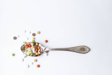 İlaç ve sağlık, ilaç, ilaç, koronavirüs, salgın, salgın konsepti - beyaz arka plan fotokopi alanı üzerinde çok renkli tablet ve kapsülleri olan gümüş bir yemek kaşığı.