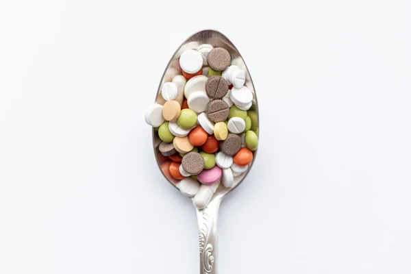 Medicine and health, treatment, pharmaceutics, coronavirus, pandemic, epidemic concept - layout one silver big tablespoon with multi-colored tablets and capsules on a white background copy space. — Stock Photo, Image