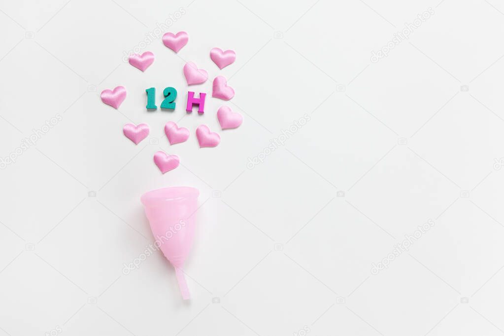 Pink menstrual cup on white background with hearts and designation of use time, 12 hours, laid out in colored numbers and letter. Concept zero waste, savings. Flat lay, copy space. Horizontal