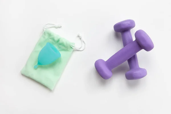 Copa menstrual turquesa en bolsa pequeña verde y mancuernas violetas sobre fondo blanco. Concepto cero desperdicio, ahorro, minimalismo, sin límites. Producto de higiene femenina para fitness, cama plana. Horizontal — Foto de Stock