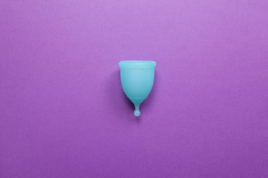 Mor arka planda turkuaz adet kupası. Sıfır israf yaşam, tasarruflar, minimalizm kavramını ele alalım. Kadın hijyen ürünleri, düz yatak, fotokopi alanı. Yatay