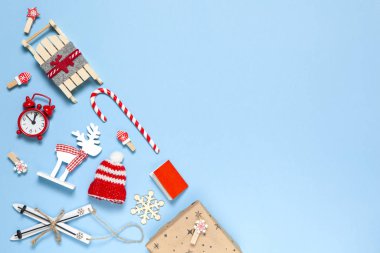 Köşedeki yaratıcı Noel kompozisyonu. Şeker kamışı, hediye, kızak, geyik, şapka, alarm saati, kayak, mandallar, kitap, mavi arka planda tahta kar taneleri, kopyalama alanı. Asgari düzeyde. Üst görünüm