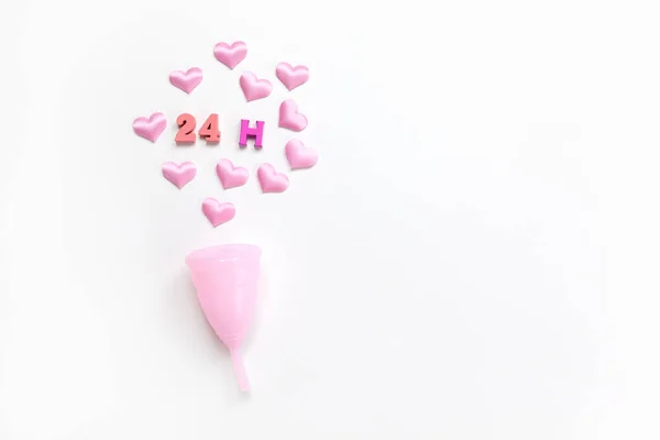Copa menstrual rosa sobre fondo blanco con corazones y designación de tiempo de uso, 24 horas, dispuestos en números de colores y letras. Concepto cero desperdicio, ahorros. Colocación plana, espacio de copia. Horizontal — Foto de Stock