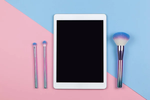 Vizeciliğin modern çalışma alanı, üst görüş. Tablet, makyaj fırçaları iki renkli arka plan pembe ve mavi, kopyalama alanı, düz yatış. Küçük işletmeler, evden çalışma, teknoloji kavramı. Yatay