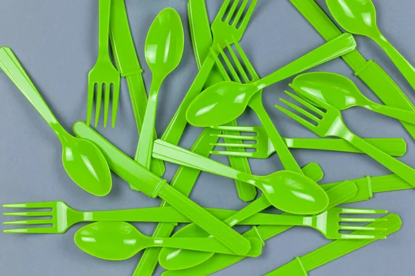 Background from reusable recyclable green forks, spoons, knifes made from corn starch on grey paper. Eco, zero waste, alternative to plastic concept. Flat lay, top view. Horizontal. Closeup