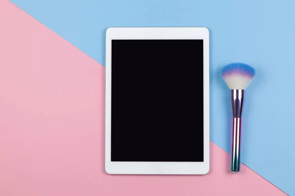 Vizeciliğin modern çalışma alanı, üst görüş. Tablet, makyaj fırçası iki renkli arka plan pembe ve mavi, kopyalama alanı, düz yatak. Küçük işletmeler, evden çalışma, teknoloji kavramı. Yatay.