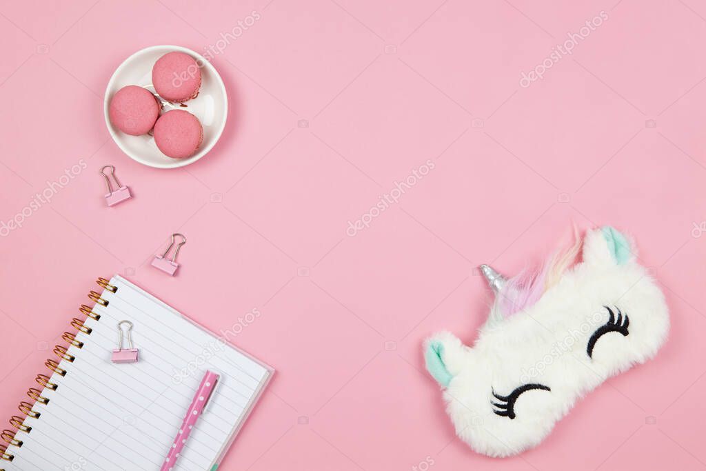 Modern female working space, top view. Cute women's or girls things, slleep mask, macarons, notepad, pen, clamps on pink backround, copy space, flat lay. Work from home concept. For blog. Horizontal.