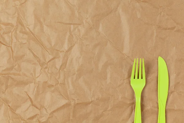 Reusable recyclable green fork, spoon, knife made from corn starch on brown crumpled craft paper, copy space. Eco, zero waste, alternative to plastic concept. Flat lay. Horizontal. Close-up.