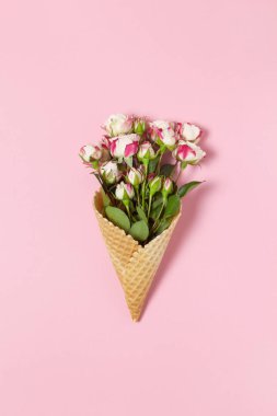 Pembe arka planda waffle külahında küçük güller, kopyalama alanı. Minimal stil düz. Tebrik kartı için davetiye. 8 Mart, 14 Şubat, doğum günü, sevgililer günü, anneler günü, kadınlar günü konsepti. Üst görünüm.