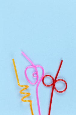 Pastel mavi arka planda içecekler için tek kullanımlık plastik renkli borular, kopyalama alanı. Şenlik konsepti, parti, doğum günü. Düz yerde, üst tarafta. Dikey. Sosyal medya için.