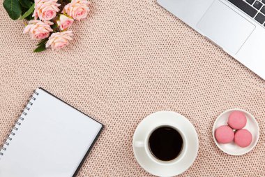 Ev kavramından çalış. Modern kadın çalışma alanı, üst görünüm. Laptop, kahve, pasta, güller, örgü örülmüş battaniye üzerine not defteri, fotokopi alanı, düz yatak. Serbest İşçi Masası. Nesnelerin çerçevesi. Yatay.
