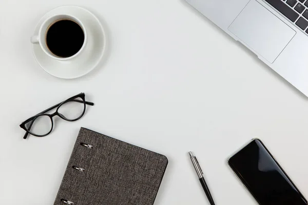 Modern unisex çalışma alanı, üst görünüm. Not defteri, kalem, kahve, akıllı telefon, gözlük, beyaz arka planda dizüstü bilgisayar, fotokopi alanı, düz yatak. Serbest İşçi Masası. Evden çalış, evde kal..