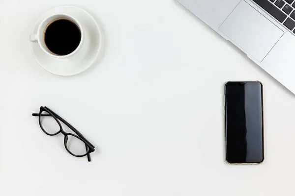 Modern çalışma alanı, üst görünüm. Laptop, kahve, akıllı telefon, beyaz arka planda bardaklar, fotokopi alanı, düz yatak. Serbest İşçi Masası. Evde çalışmak, evde kalmak, teknoloji kavramını kullanmak..