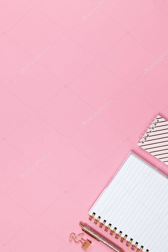 Modern female working space, top view. Notebooks, pen, clamp on pink backround, copy space, flat lay. Desktop of freelancer, student. Work from home, back to school, education concept. Vertical.