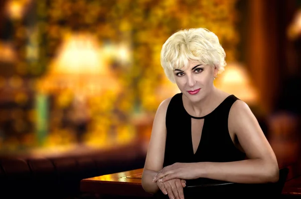 Woman in cocktail dress sitting on blurred background of cafeteria inside — Stock Photo, Image