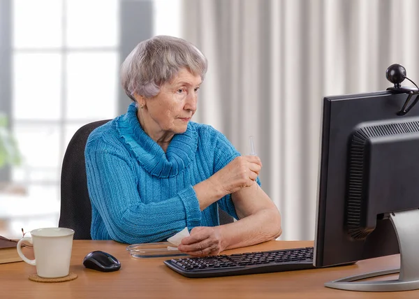 Пожилая женщина делает внутримышечную инъекцию перед монитором компьютера — стоковое фото