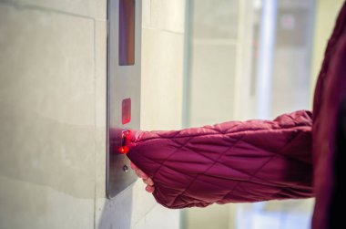 Woman panicked when she needed to press an elevator button. She pulled the sleeve nylon down jacket on her hand for fear of having contracted the coronavirus.  clipart