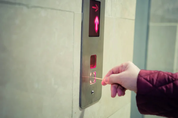 A woman pushing an elevator button with a toothpick instead of using her hand. Because this woman is caught with coronavirus panic