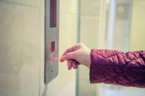 Woman presses with a toothpick the lift button for avoidance to catch a coronavirus