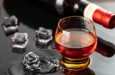 Şarap kadehli bir şişe kırmızı şarap. Siyah yansımaya su sıçrıyor ve damlatıyor..